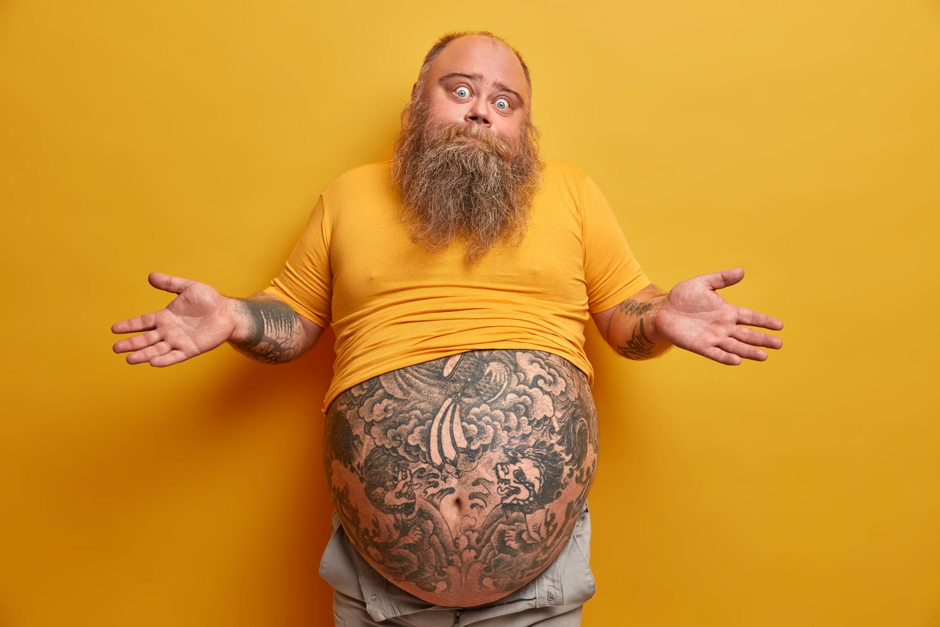fat man with tatto'ed belly holding his hands up, looking confused